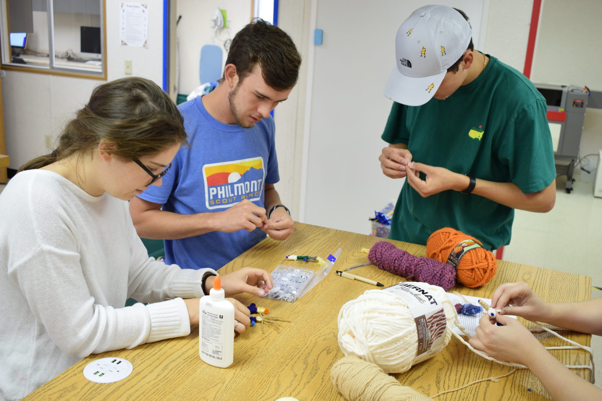 A group of three students work on a crafting activity with yarn and glue.
