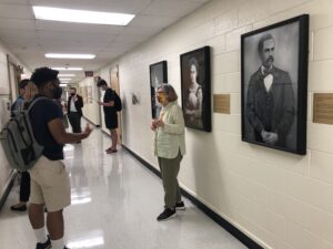 Photo from the portrait unveiling event showing event attendees talking while standing by the paintings