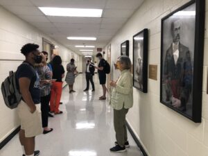 Photo from the portrait unveiling event showing event attendees talking while standing by the paintings