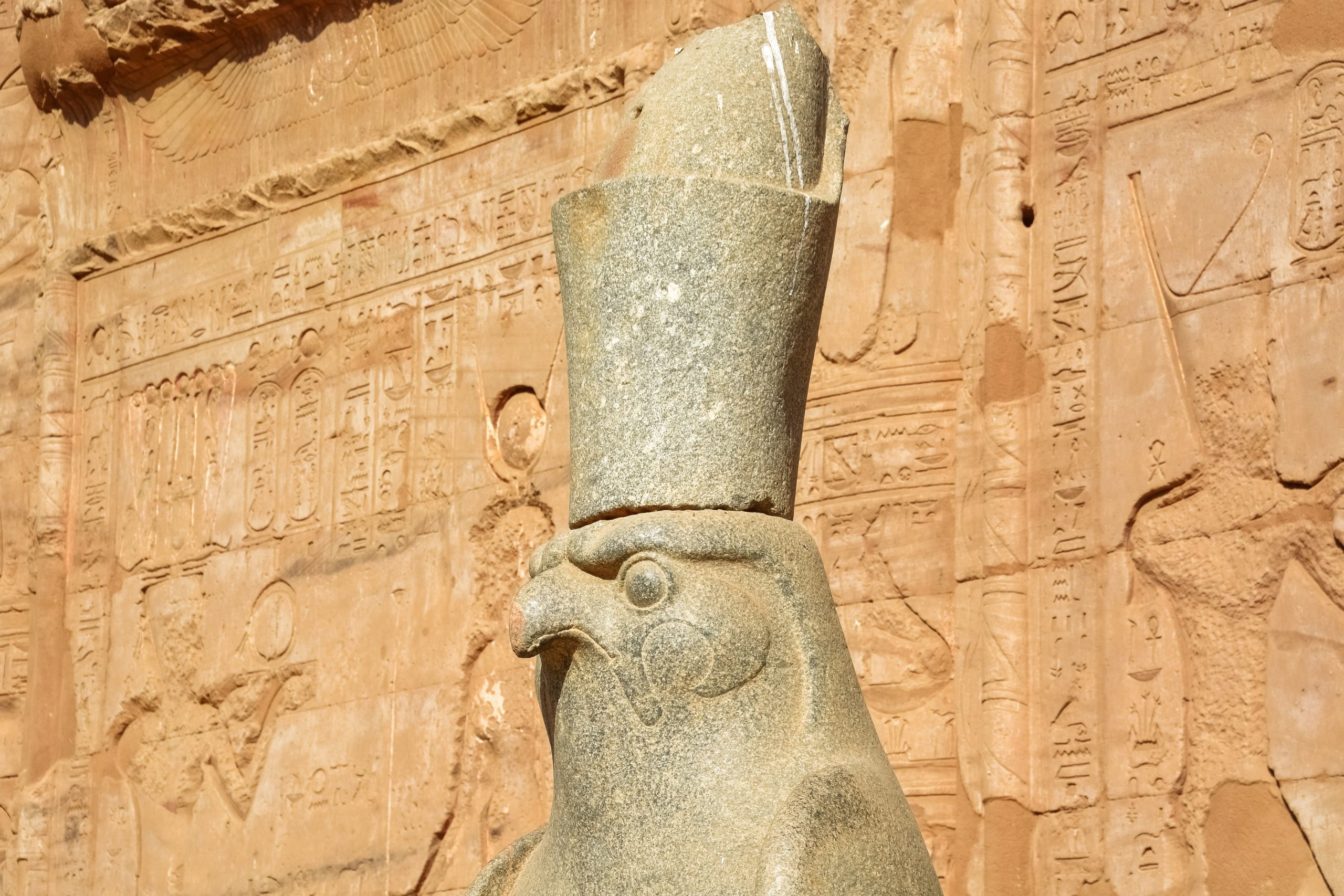 Statue from ancient world in foreground. Background is a wall with images etched into it. 