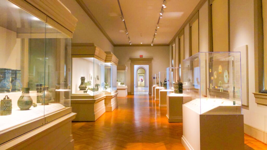 Image of museum room with multiple exhibits with historic items protected behind glass.  