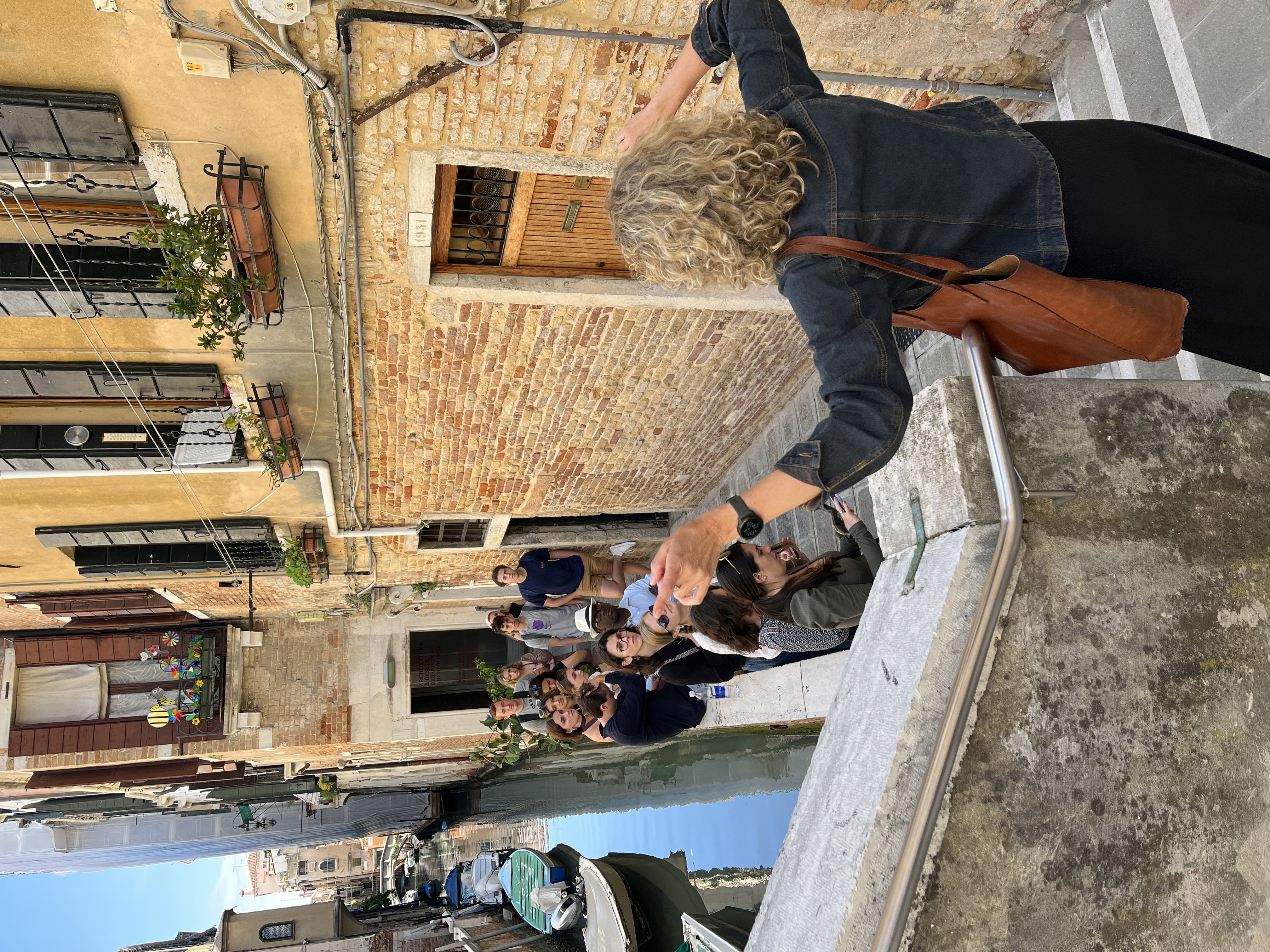 Venice, 2023: A professor with their back to the camera speaks to a group of students alongside a canal in Venice.