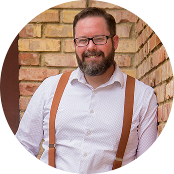 Profile picture of Seth Jeppesen: a white man with brown hair, glasses, salt-and-pepper full beard. He is smiling and leaning against a brick wall. He has a white button-up shirt and tan suspenders.