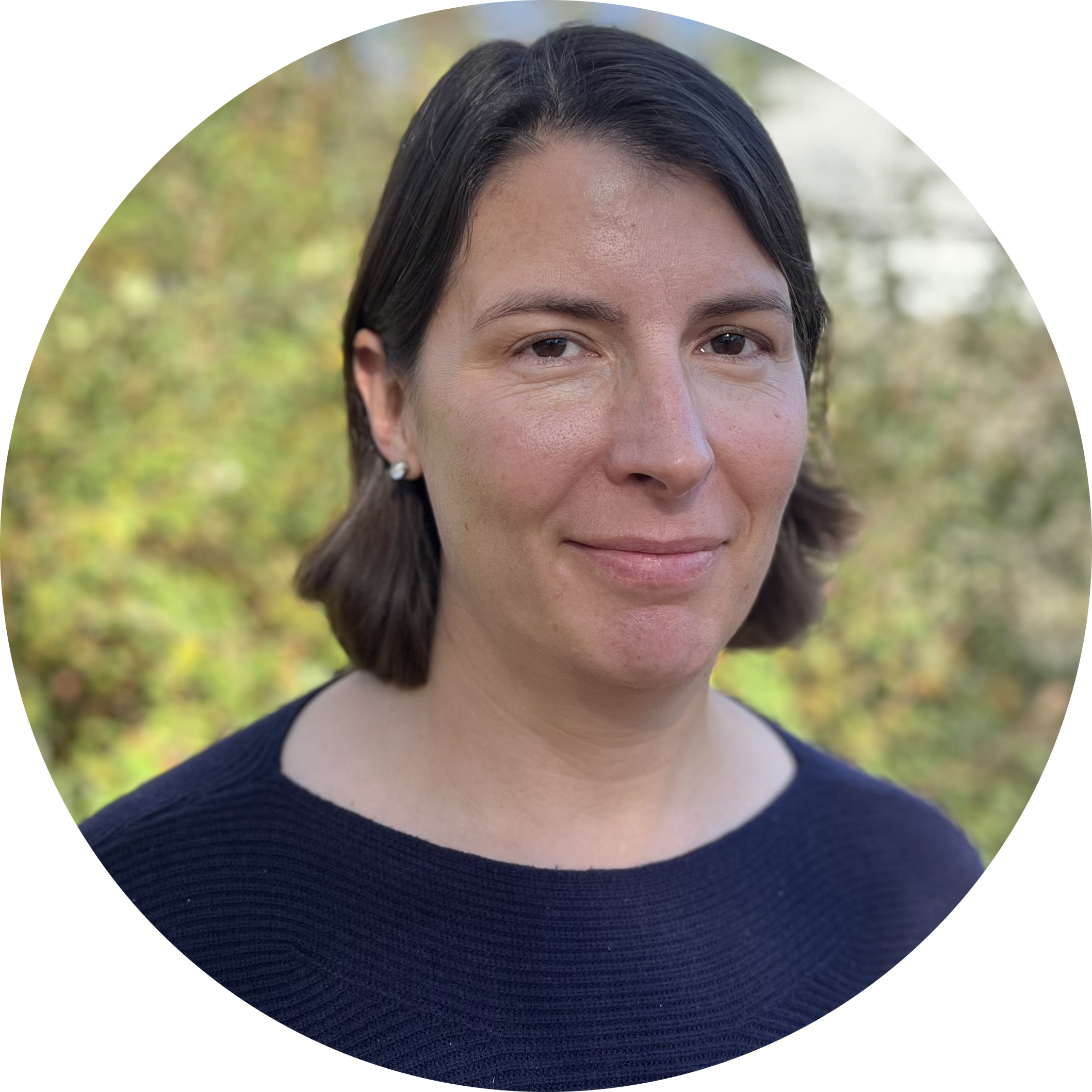 Profile picture of Erin K. Moodie: a white woman with shoulder-length straight dark brown hair tucked behind her ears. She is wearing a navy top. The background, blurred out, is of trees with mostly green leaves, some hints of early fall's yellow, red, and orange.