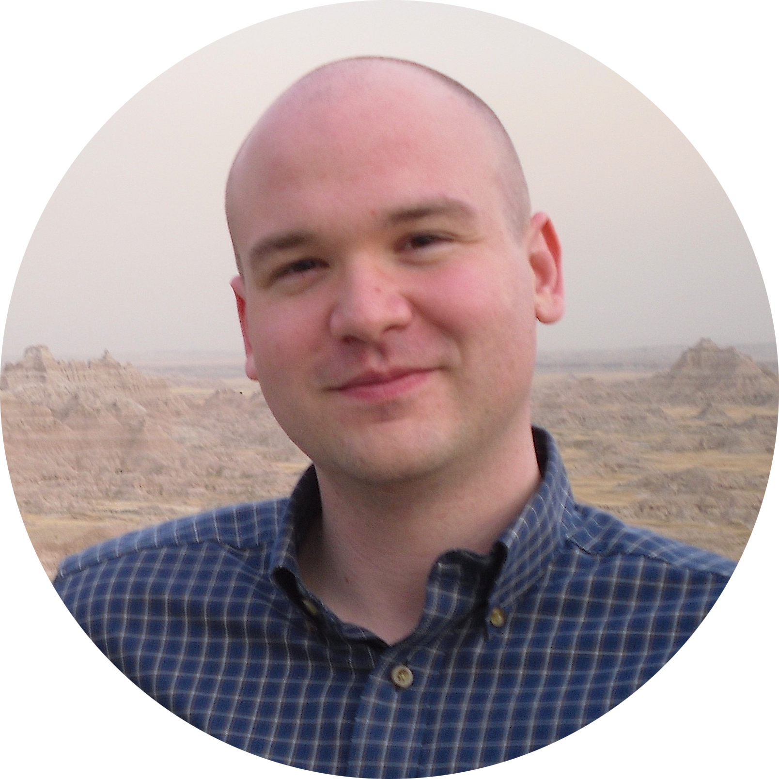 Profile picture of Christopher B. Polt: a bald white man gently smiling at the camera and wearing a blue checked button-up. The background is of a rocky desert landscape.