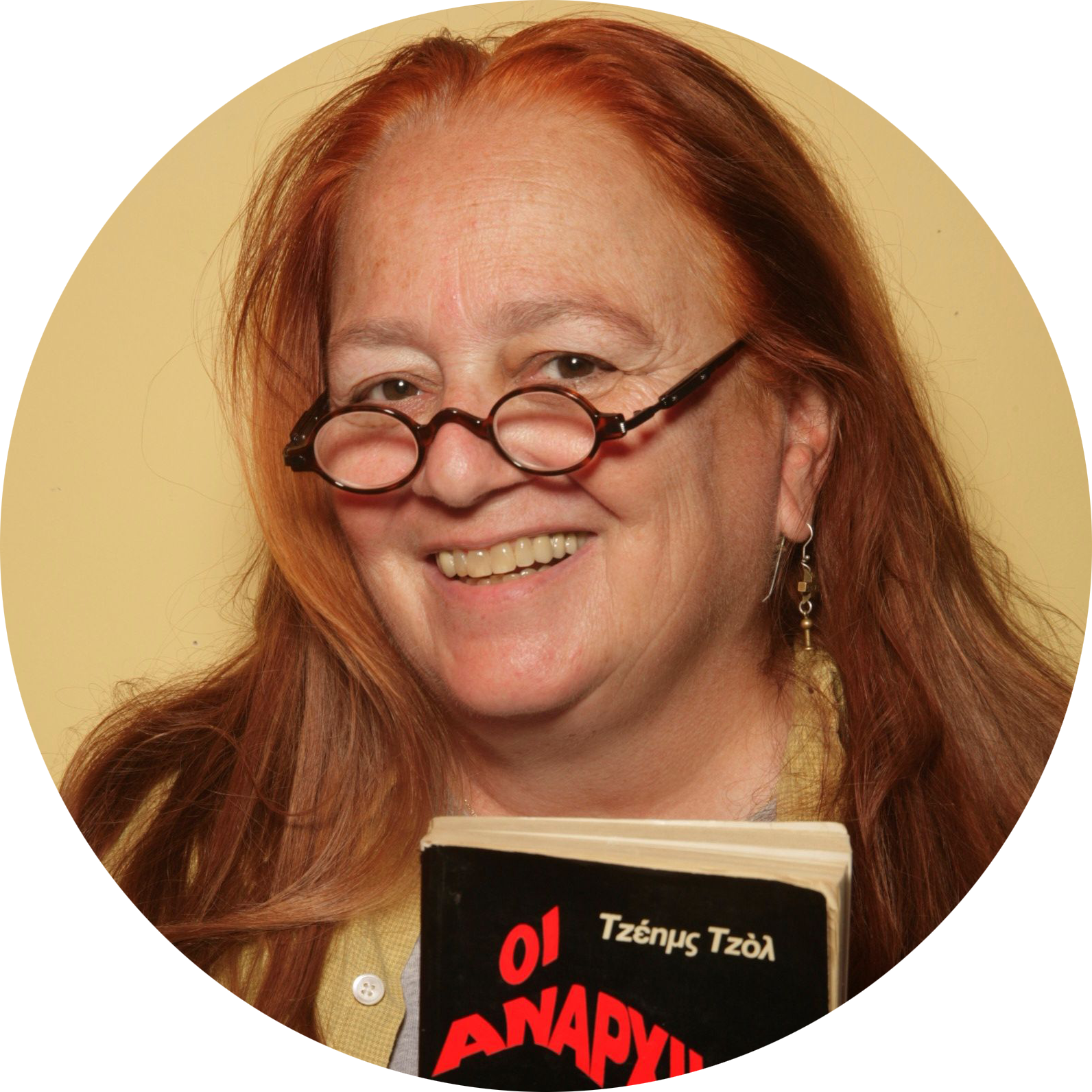 Profile picture of Amy Richlin: a white woman with red hair and glasses. She is smiling and holding up a book in modern Greek, by the author Τζέημσ Τζὸλ and with the title Οι Αναρχικοι