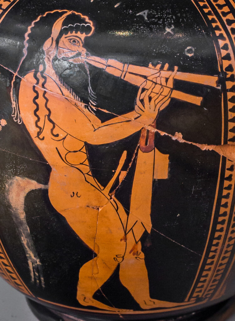 A portion of an ancient Greek red-figure vase painting of a naked, erect satyr with long black hair and a beard playing a pair of auloi.