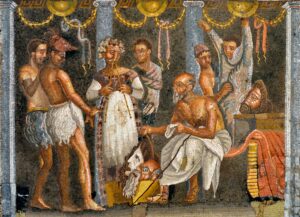 An ancient mosaic of actors backstage preparing for a play. Seven men, all but one standing, in various stages of dress and costume. One is playing a set of double pipes. The seated one is pulling a mask from a box of masks. One is helping another put on a shaggy full-body costume. A mask sits on a table to the right. The dominant colors are white, yellow, red, blue, black, gray, and tan (this last for the skin color of the actors).