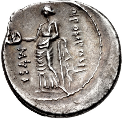An ancient silver coin depicting the muse of comedy. A stick figure of a woman wearing a chiton and holding a smiling mask in her hand. Hard-to-decipher Greek letters running vertically in front of and behind the figure.