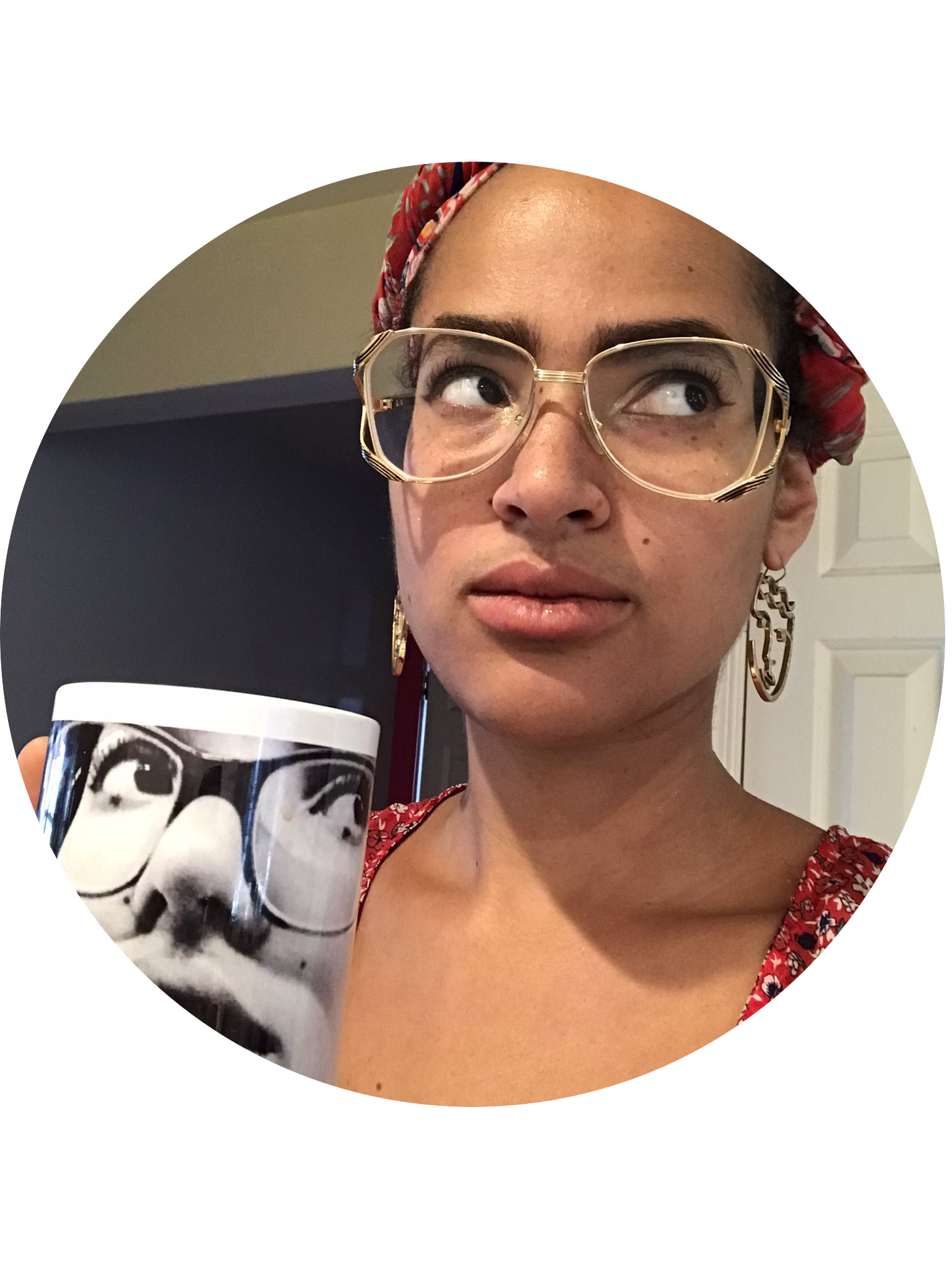 Profile picture of Vanessa Stovall: a woman with light-to-medium-brown skin tone and black hair under a red hair covering. She is wearing large-frame gold-frame glasses and figural dangly earrings. Her eyes are looking up and to her left. She is holding by her face in her right hand a coffee mug decorated with a close-up photo of her own face, wearing glasses and with eyes looking up and to the left.