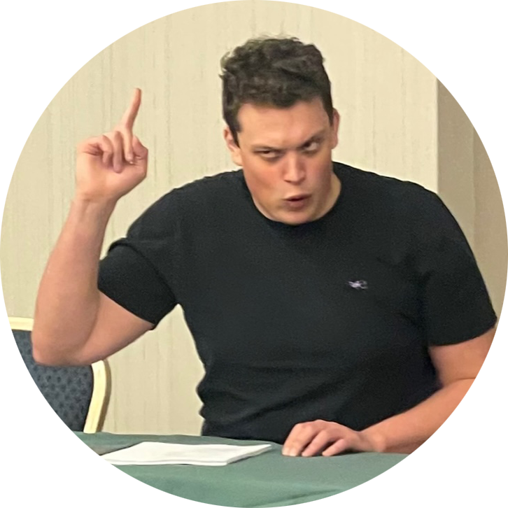 Profile picture of Joe Droegemueller: a white man with black hair. He is wearing a black t-shirt. He is pointing at the ceiling with his right hand and speaking with a suspicious or stern look on his face.