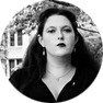 Profile picture of Emma Pauly: a black-and-white photo of a white person with long dark hair. They are looking pensively into the distance.