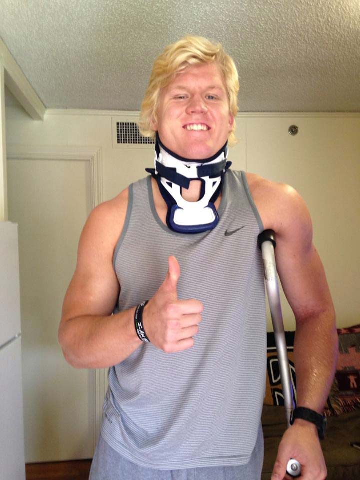 Zach with neck brace standing with one crouch under his left arm and right hand giving a thumbs up