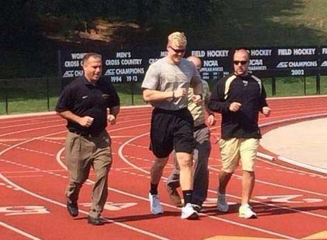 Zach jogging on track unaided by crutches and with several couches running with him