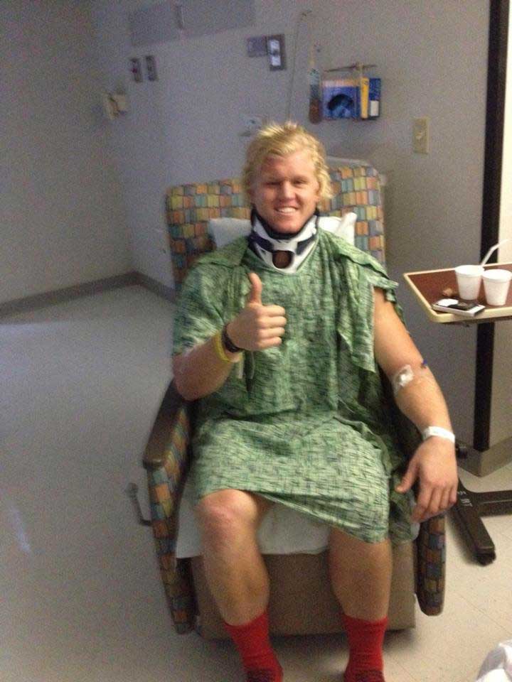 Zach Gordon in hospital chair with neck brace giving a thumbs up.
