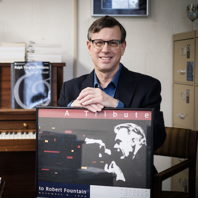 A seated man smiles next to a piano. Brian Gorelick was director of the Wake Forest University Choral Programs from 1984-2020.