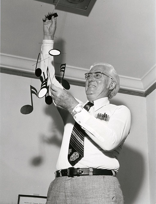 Black and white photo of a man installing a mobile depicting musical notes. Thane MacDonald was director of the Wake Forest University Choral Programs from 1941-1975.