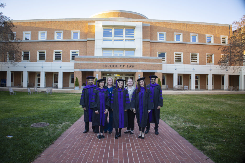 A small group of Wake Forest Law graduates in graduation garb standing in front of Worrell Professional Center Building, home to Wake Forest Law.