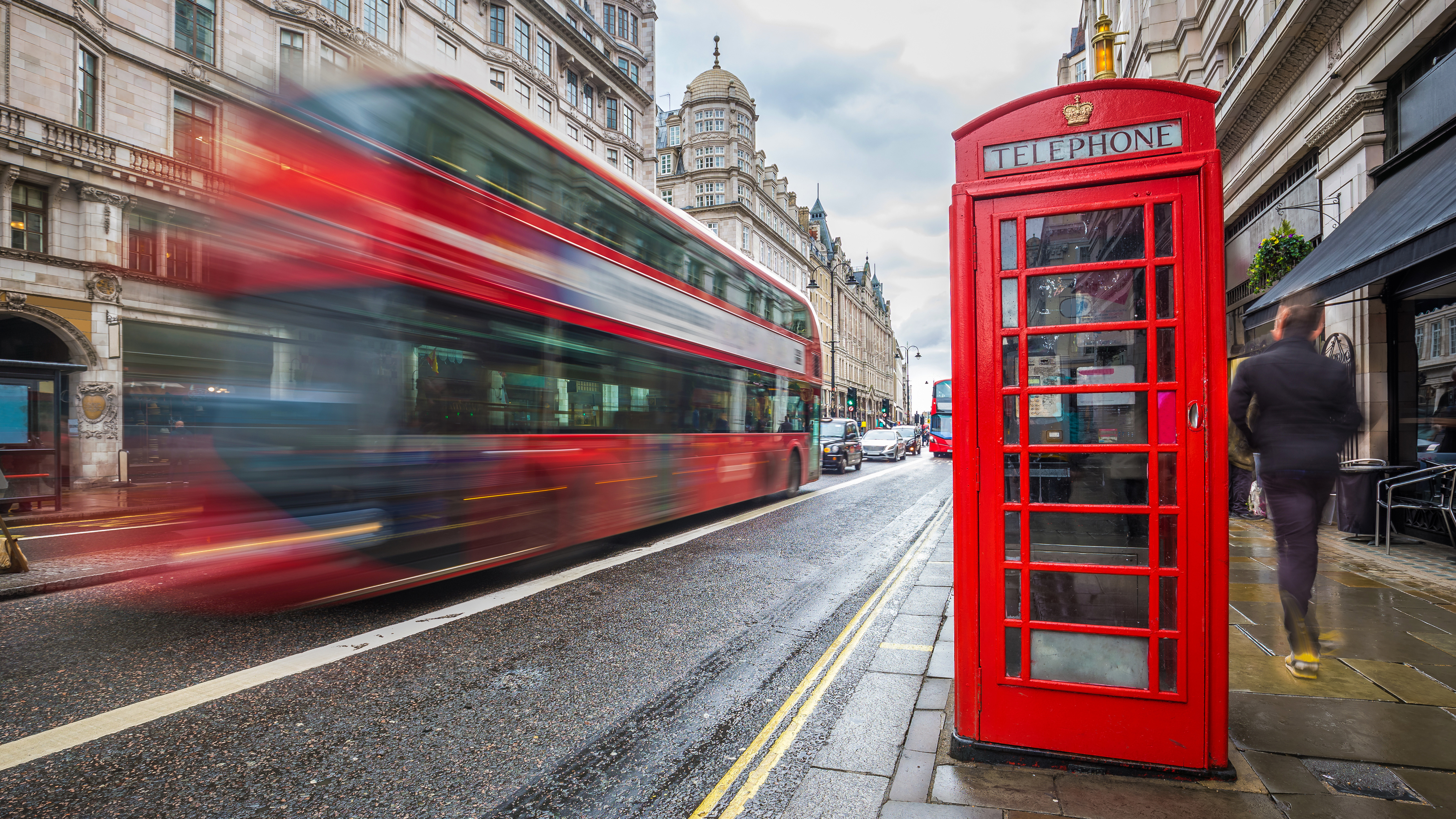 A red bus driving past a red phone booth in London.
