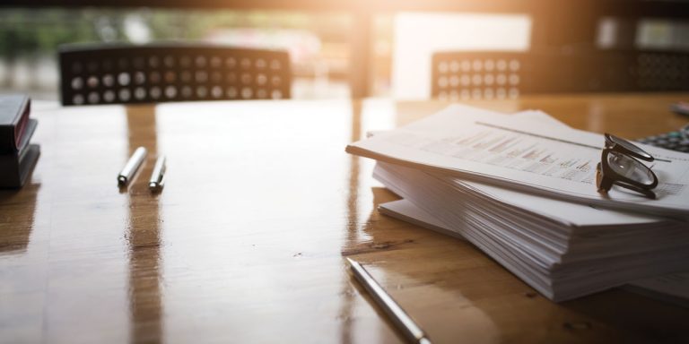 A stack of papers on a desk with two pens.