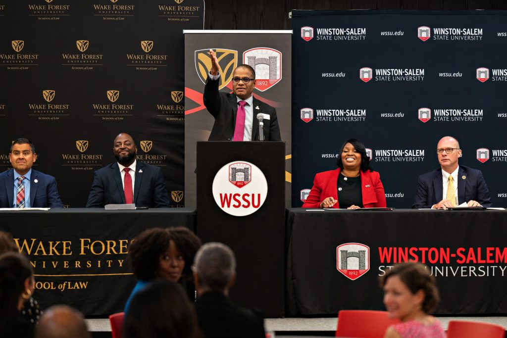 WSSU Dean Manju Bhat stands at the podium and motions to the audience to thank them