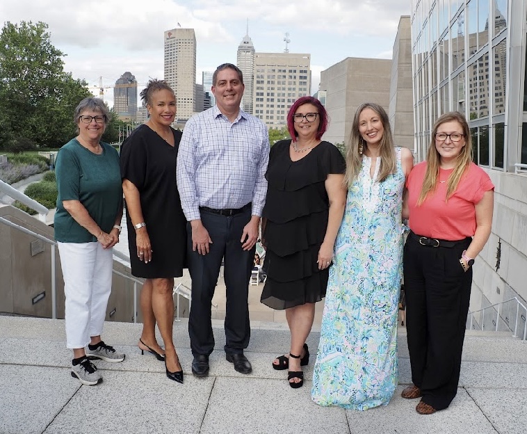 Professor Abby Perdue posing with five Legal Writing Institute members (men and women) in front of a cityscape and river