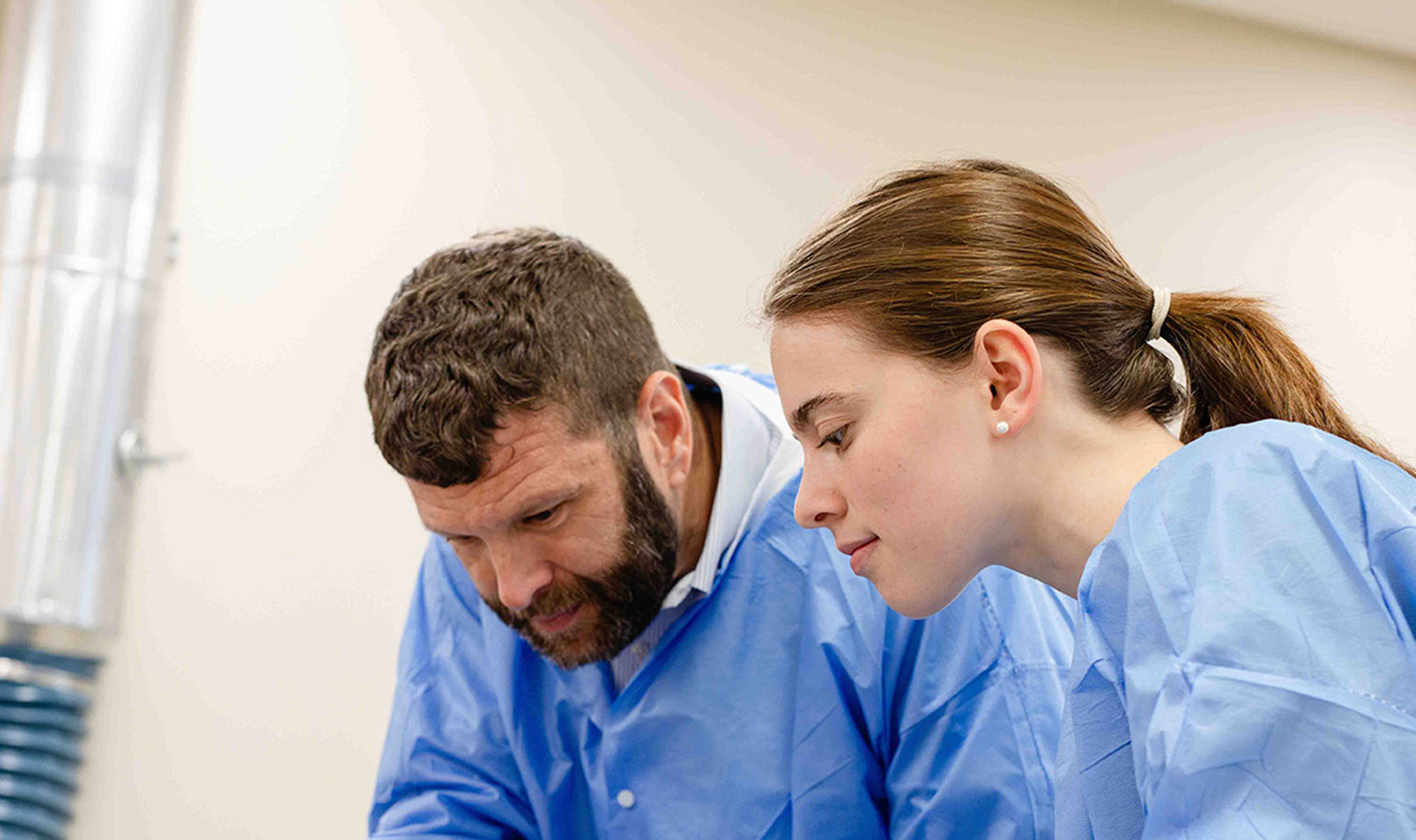 Dr. Ted Eaves and a student both in medical scrubs bending over a cadaver (not pictured).