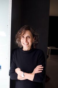 Photo of Elizabeth Kolbert smiling with her arms crossed, leaning against a wall.