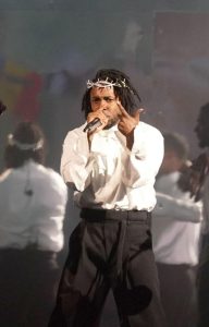 Figure 1: Kendrick Lamar on stage wearing a white shirt, black pants, and a crown of thorns.