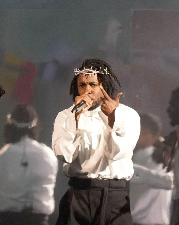 Figure 1: Kendrick Lamar on stage wearing a white shirt, black pants, and a crown of thorns.