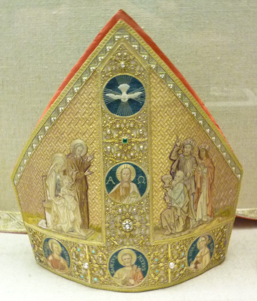Figure 3. A nineteenth century mitre embellished with precious gems and holy figures, including Joseph, Mary, and the infant Jesus on the left and the Three Kings or Wise Men on the left. From the Treasury of the Cathedral of Trier. Photo by Tom Lemmons. CC by 4.0 International.