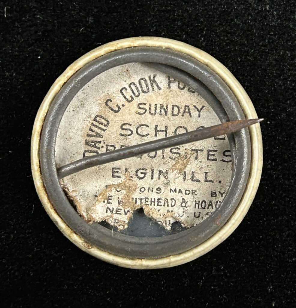 Figure 7: Back of pinback button that shows the partnership between David C. Cook Publishing and Whitehead & Hoag. Photo by author.