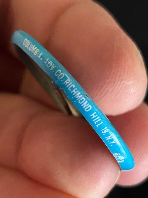 Blue side of button with the manufactured of the button labeled