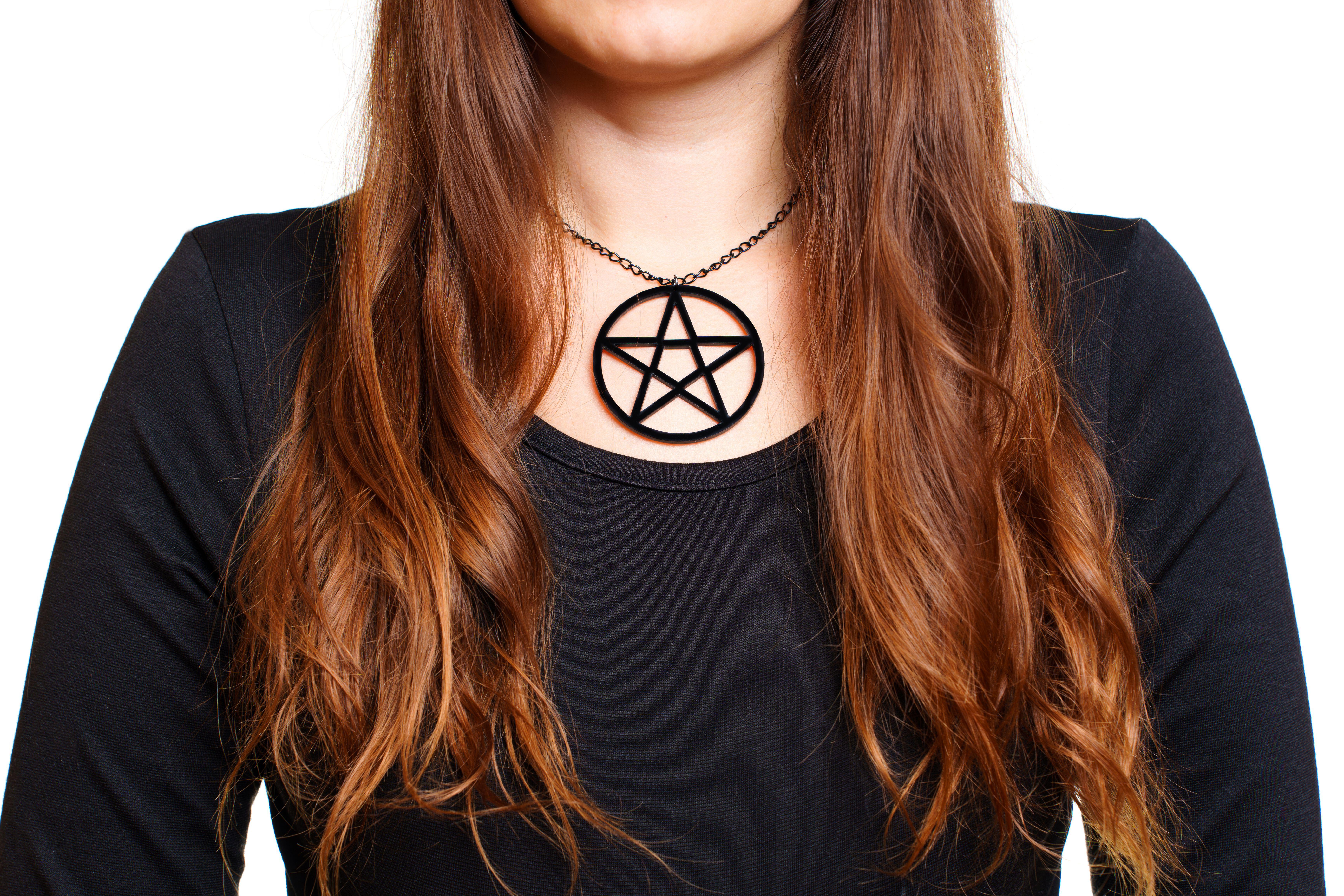 Crop body view of a woman in black long sleeve dress wearing a large pentagram pendant isolated on white background.