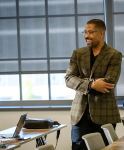 Photo of Corey D.B. Walker smiling with his arms crossed at the front of a classroom