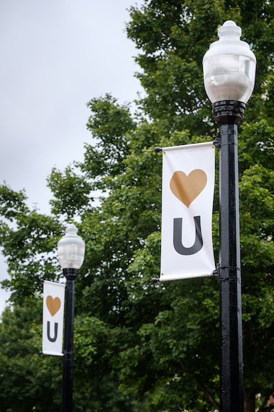 Two lamp posts with white banners showing the "Show Humanitate" logo of a gold heart and the letter "U"