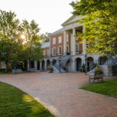 Photo of Reynolda Hall as seen from Hearn Plaza with the sun peeking through the trees