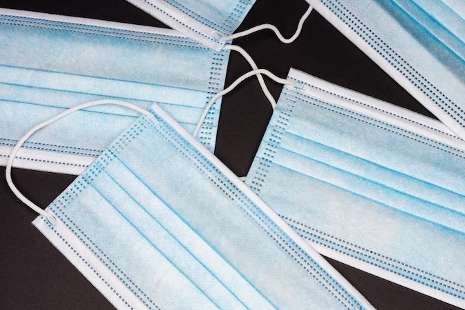 Several blue, disposable surgical masks on black background