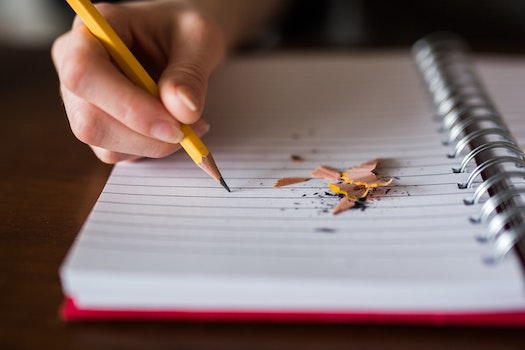 Photo of student holding a pencil and writing on a notebook that has pencil shavings on it