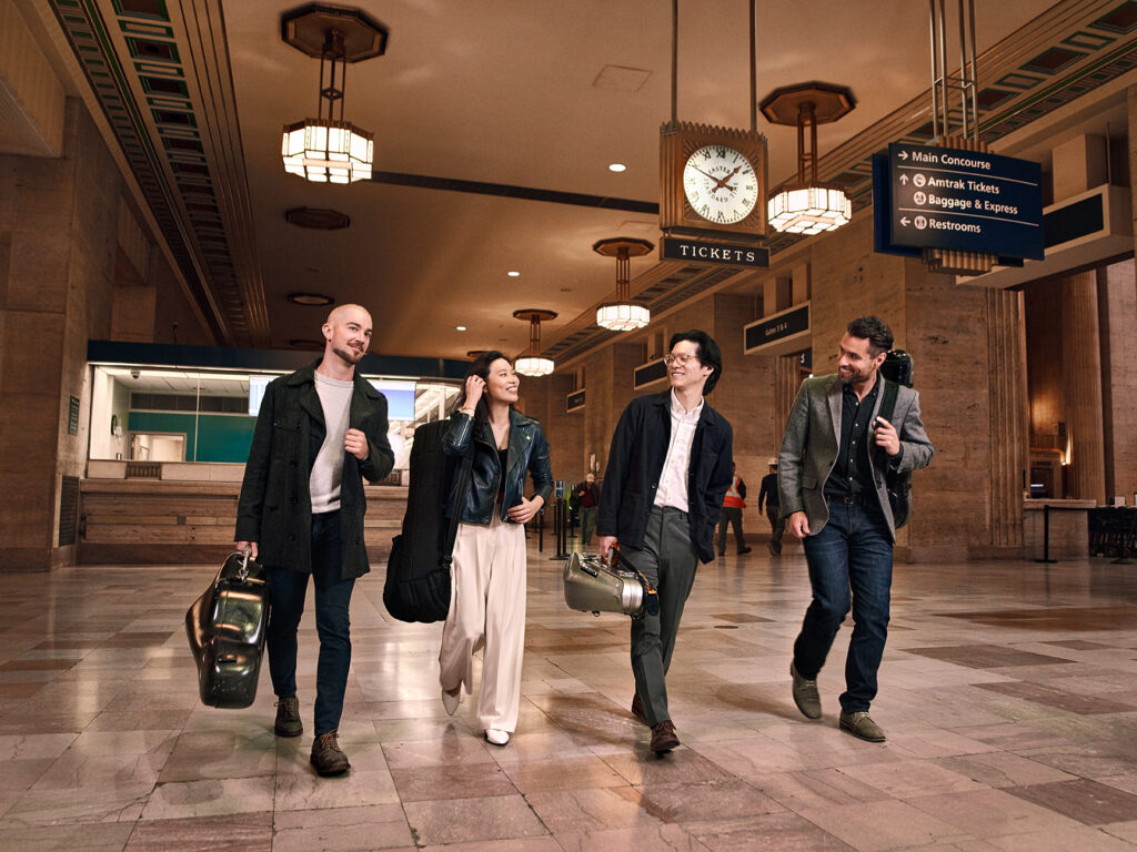 Four people walking carrying string instruments