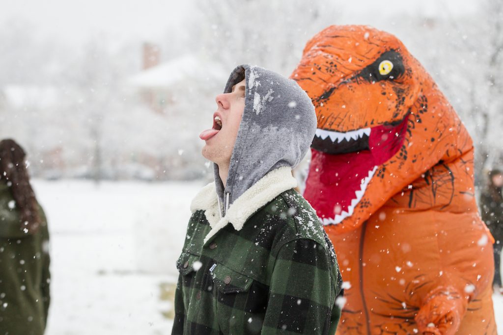 Student in dinosaur costume sneaks up on student on the Quad in the snow